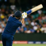 Batsman completing a lofted drive under floodlights